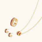 Three-piece jewelry set featuring 14K gold plated pieces with deep red cubic zirconia stones and clear crystals on cream background.