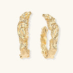 Close-up of sculptural hoop earrings with organic molten texture in silver and gold finishes on white background