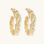 Close-up of sculptural hoop earrings with organic molten texture in silver and gold finishes on white background
