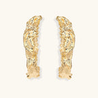 Close-up of sculptural hoop earrings with organic molten texture in silver and gold finishes on white background
