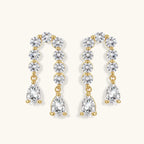 Gold-plated earrings with vertical line of clear crystals and teardrop pendants on neutral background